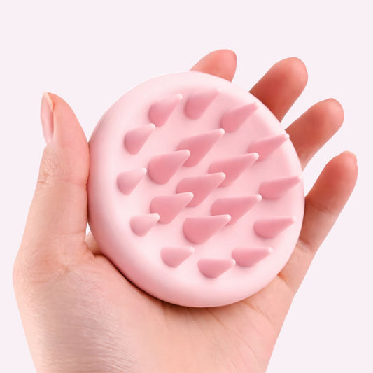 Close-up of a hand holding a small pink scalp massager against a light background