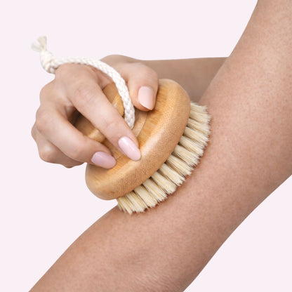 Hand using a wooden body dry brush with bristles on an arm against a light background