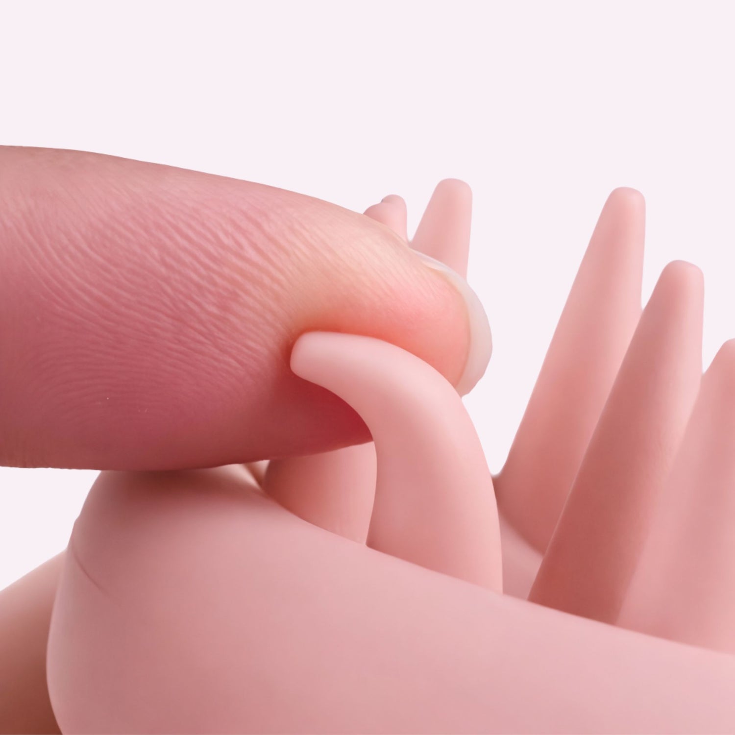 Close-up of a hand holding a small pink scalp massager against a light background